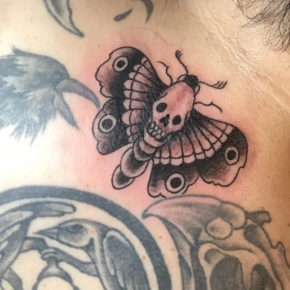 Traditional death's-head moth tattoo with a skull on its thorax at the base of the neck