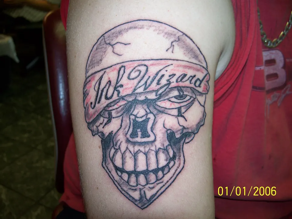 Black linework skull tattoo with a banner on the upper arm