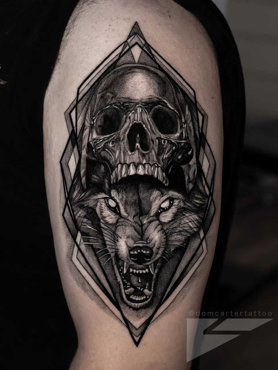 Black and grey skull and wolf tattoo with a geometric frame on the upper arm
