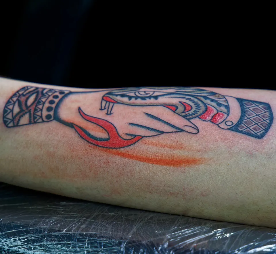 Traditional tattoo of a snake biting a hand on the forearm