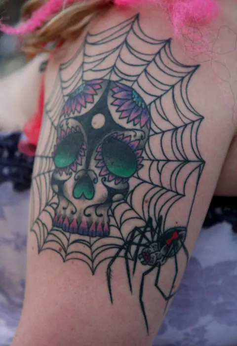 Sugar skull inside a spider web with a black widow spider on the arm